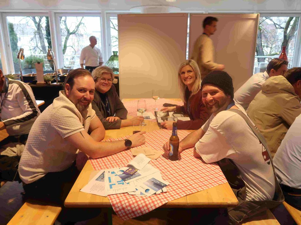 Zwei Frauen und zwei Männer sitzen an Biertisch mit karierter Tischdecke.