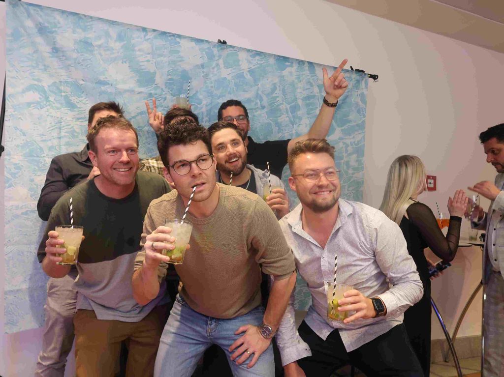 Männer mit Caipirinha-Gläsern und Strohhalmen lachen fürs Gruppenbild.