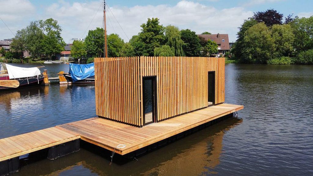 Die schwimmende Sauna von Außen mit Segelboten im Hintergrund.