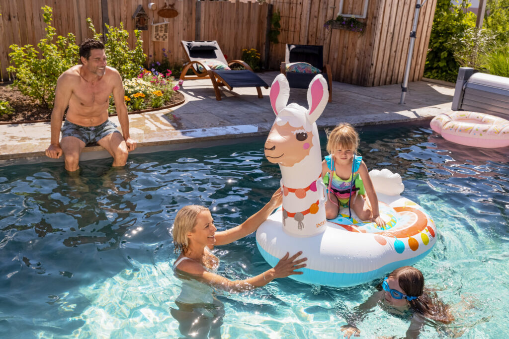 Zwei Erwachsene und zwei Kinder planschen mit einem Schwimmtier im Pool.
