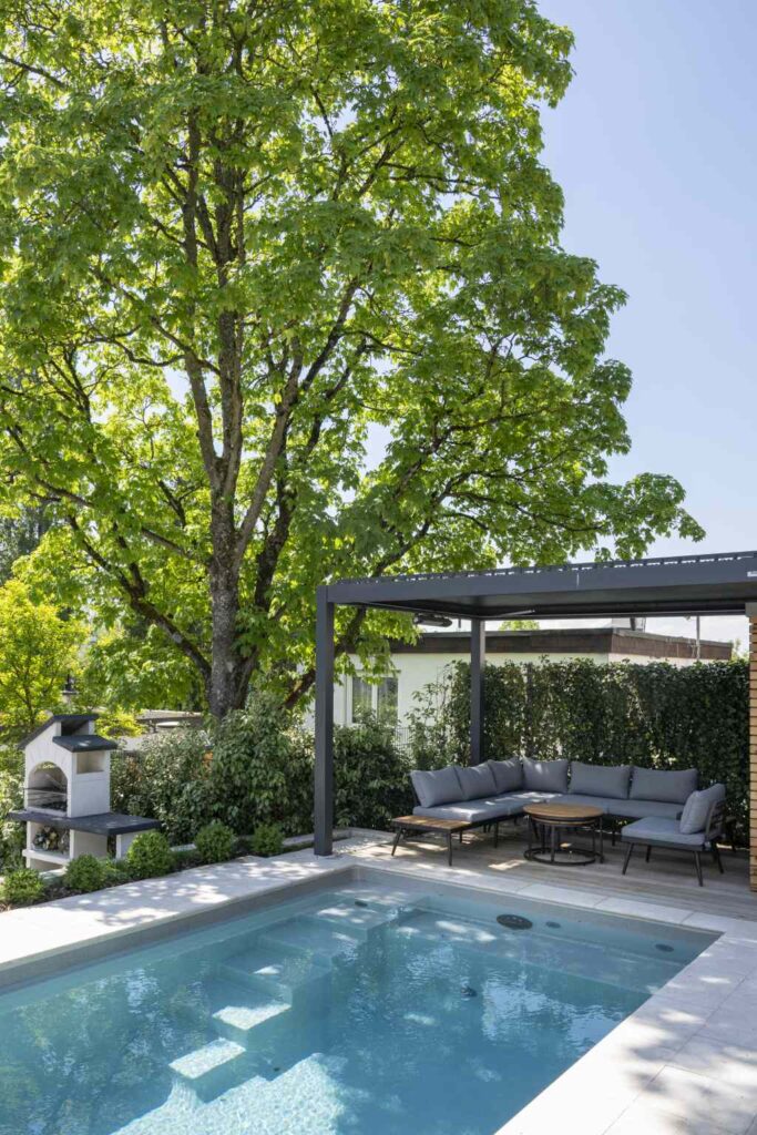 Eine Pergola spendet Schatten am Pool. Darunter steht eine Sitzgruppe.